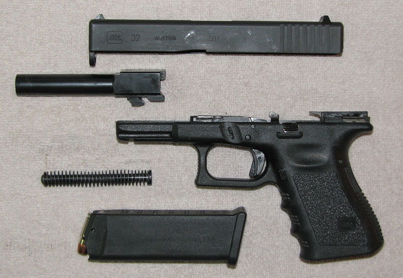 Field-stripped Glock pistol includes slide assembly, receiver/frame, barrel, recoil spring/rod assembly, and magazine. Further disassembly should only be performed by a certified armorer.