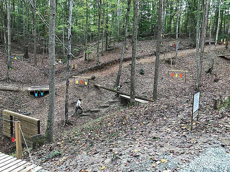 EST deputy charges through assault course with sidearm. Hits were required before advancing, and performance was timed. Steel targets on other side of road are situated for long-gun training. Flat trajectory and plunging fire challenges are evident.