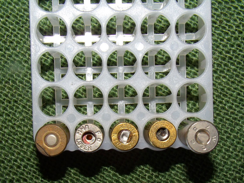 Case rim on cartridge has been partially sheared off. Other factory rounds show crushed primers, primer with a hole in it, and one round with no primer at all.