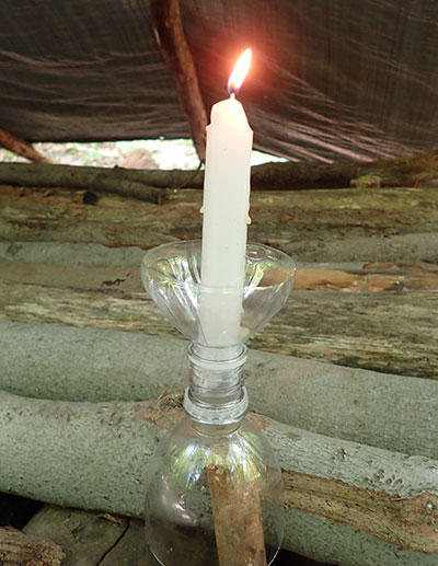 Author uses candle holder on his pole bed, held in place with a wooden stake pressed firmly in the ground. It offers candle light that is not going to get knocked over easily.