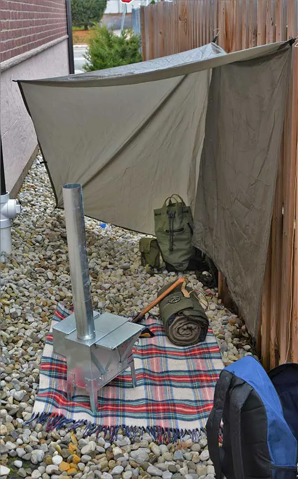 Rocks underfoot may not be the best environment to build a shelter, though proper water drainage and brick make this potential shelter site worthwhile. Tarp blocks possible wind entering from holes in fence. Short overhang gives additional wind resistance when needed.