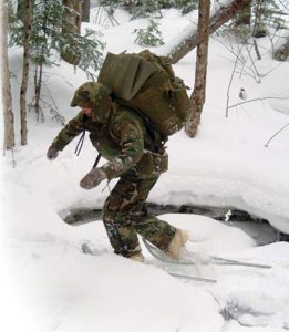 Student-at-U.S.-Navy’s-SERE-school-snowshoes-across-frozen-creek-during-training-in-Rangely,-Maine