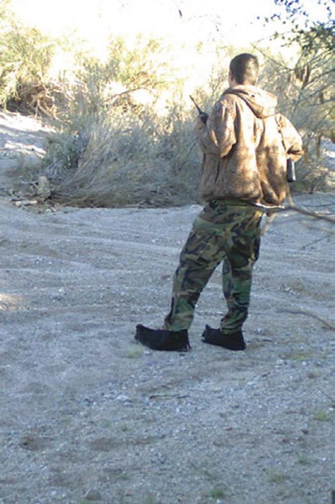 Cartel-scout-surveys-his-area,-radio-in-hand,-binoculars-on-his-right-hip